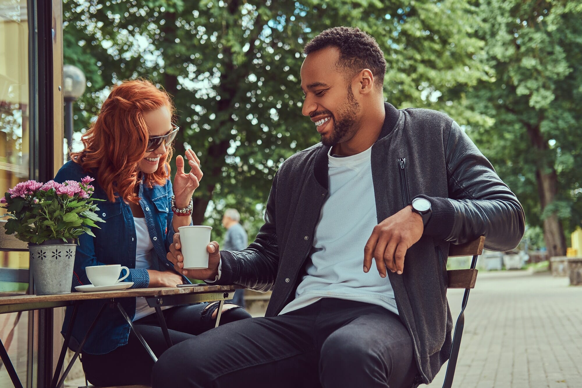 A couple dating drinking coffee, sitting near the coffee shop. Outdoors on a date.